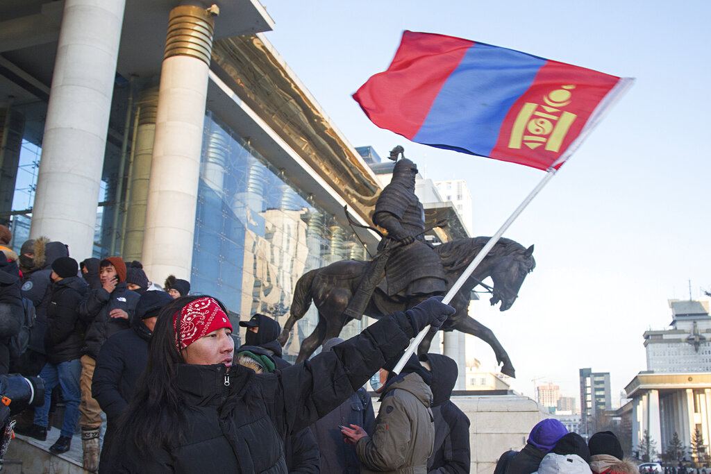 A protester waves a Mongolian national flag as protesters gather on the steps of the State Palace in Ulaanbaatar in Mongolia on Monday, Dec. 5, 2022. Protesters angered by allegations of corruption linked to Mongolia's coal trade with China have stormed the State Palace in the capital, demanding dismissals of officials involved in the scandal. (AP Photo/Alexander Nikolskiy)