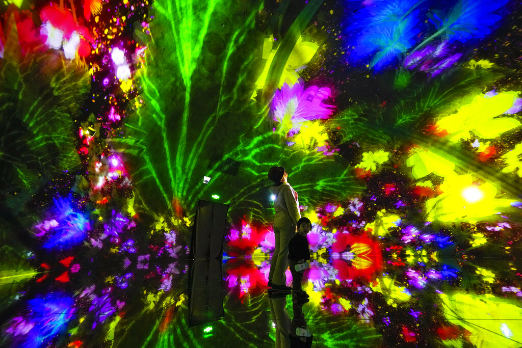 A woman and a child experience a digital installation that features projection of flowers titled 