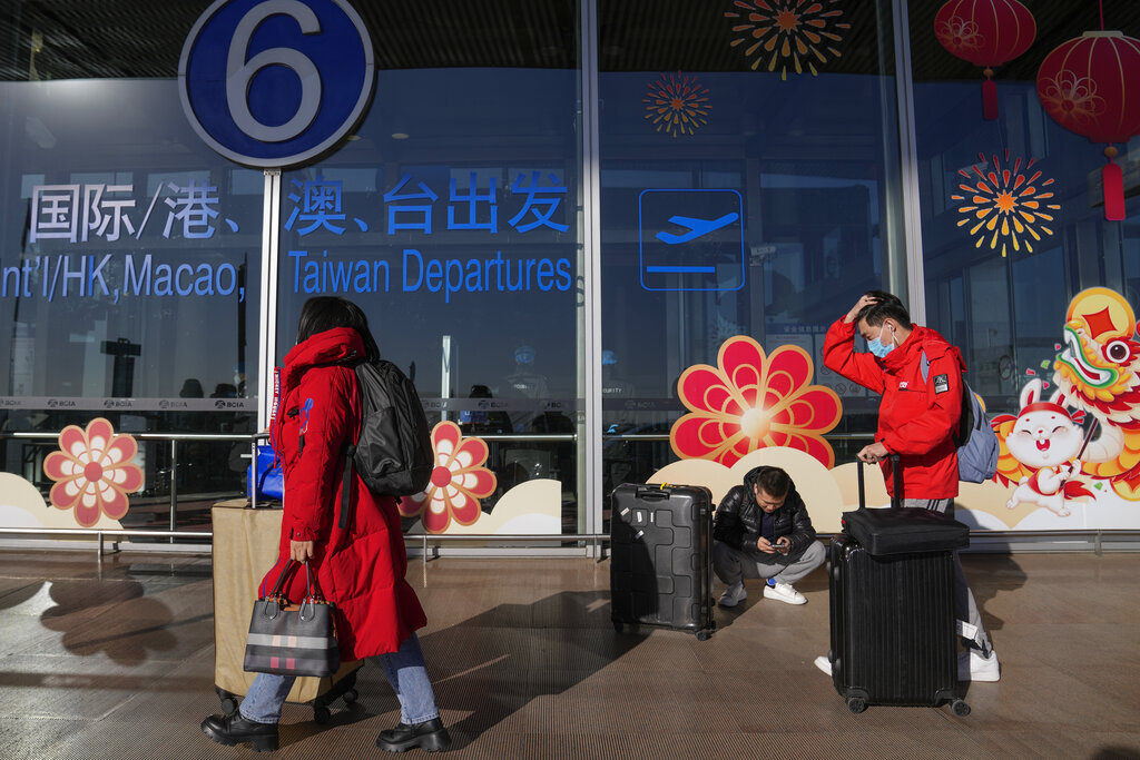 Traveller wearing face masks with their luggage walk through the international flight departure terminal entrance gate at the capital airport in Beijing on Dec. 29, 2022. Australia and Canada have joined a growing list of countries requiring travelers from China to take a COVID-19 test prior to boarding their flight, as China battles a nationwide outbreak of the coronavirus after abruptly easing restrictions that were in place for much of the pandemic. (AP Photo/Andy Wong)