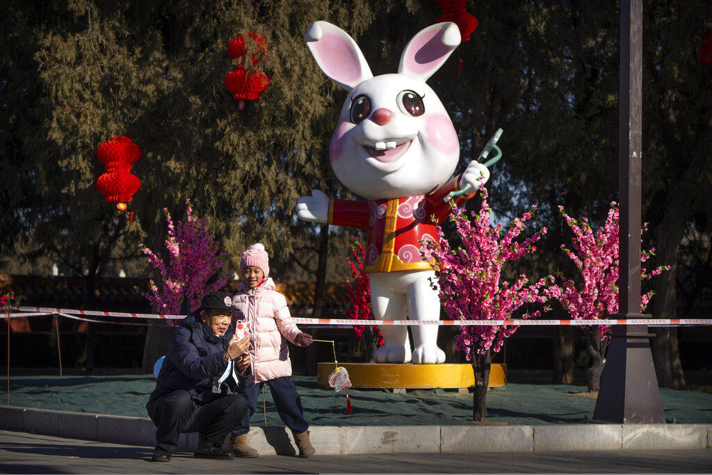 A man and girl pose for a selfie in front a of a statue of a rabbit for the upcoming Lunar New Year at a public park in Beijing, Friday, Jan. 20, 2023. The Year of the Rabbit officially begins on Jan. 22. (AP Photo/Mark Schiefelbein)