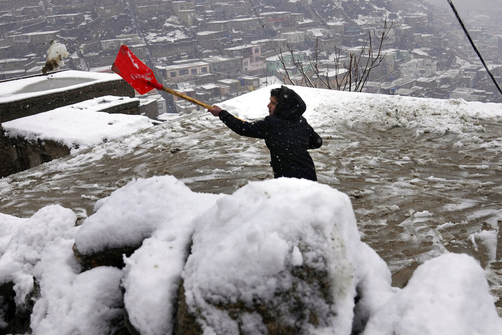A Afghan boy clears the snow from the roof of his house during rainy and snowy weather, on a hilltop overlooking Kabul, Afghanistan, Tuesday, Feb. 22, 2022. (AP Photo/Hussein Malla)