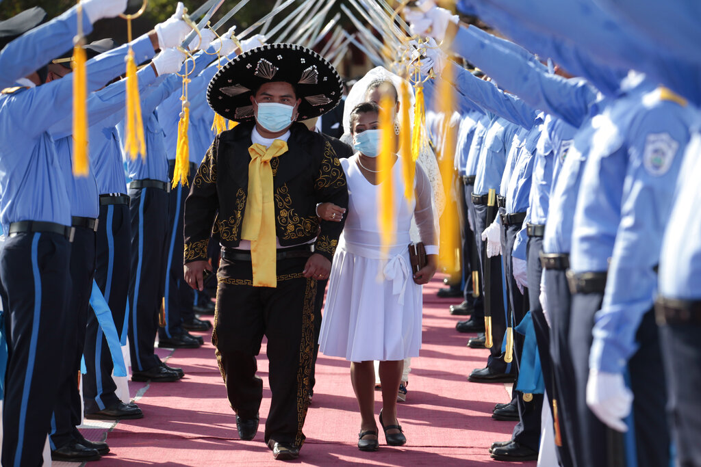 A couple walks under an aisle of police cadet swords during a mass wedding in Managua, Nicaragua, Sunday, Feb 14, 2021. Around 400 couples said 