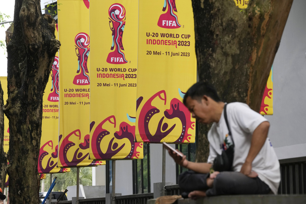 A man checks his mobile phone near banners of FIFA U-20 World Cup in Jakarta, Indonesia, Thursday, March 30, 2023. Indonesia was stripped of hosting rights for the Under-20 World Cup on Wednesday only eight weeks before the start of the tournament amid political turmoil regarding Israel's participation. (AP Photo/Dita Alangkara)