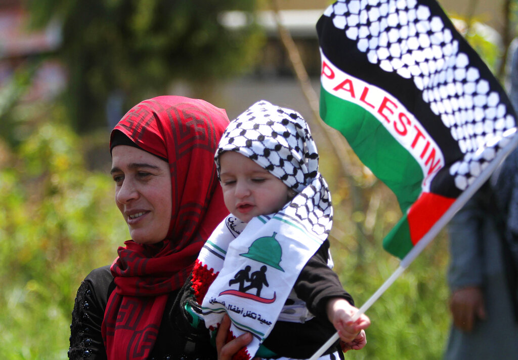 CORRECTS SECOND SENTENCE - A Palestinian woman who lives in Lebanon carries her child with the Palestinian flag during a protest marking the 67th anniversary of Nakba, or Catastrophe, in front of the United Nations peacekeepers (UNIFIL) headquarters in the costal town of Naqoura, southern Lebanon, Friday, May 15, 2015. Palestinians annually mark the Nakba Day, or the Day of the Catastrophe, when hundreds of thousands of Palestinians fled, or were expelled from their homes during the first Israeli-Arab war in 1948. (AP Photo/Mohammed Zaatari)