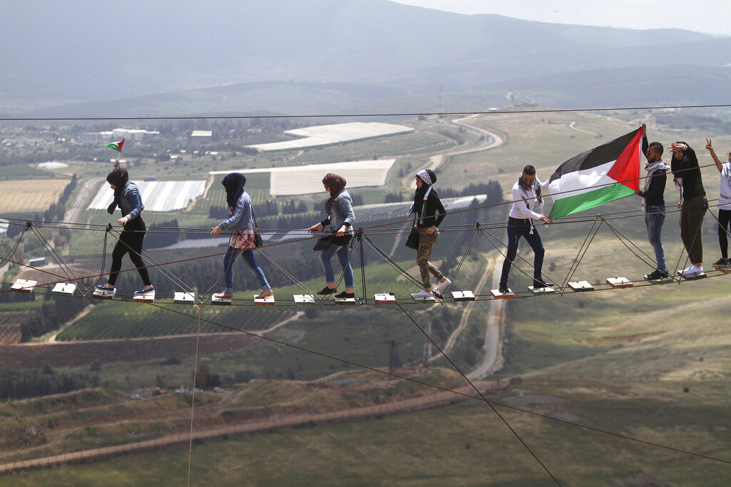 A Palestinian living in Lebanon with a small Palestinian flag leads other women as men hold up a bigger one on a suspension bridge, overlooking Israeli settlements during a protest marking the 67th anniversary of Nakba, or Catastrophe, at Iran park in the southern Lebanese-Israeli border village of Maroun el-Rass, Lebanon, Thursday, May 14, 2015. Protesters commemorated on Thursday the dispersal of Palestinians over Israel's creation during the first Israeli-Arab war in 1948. (AP Photo/Mohammed Zaatari)