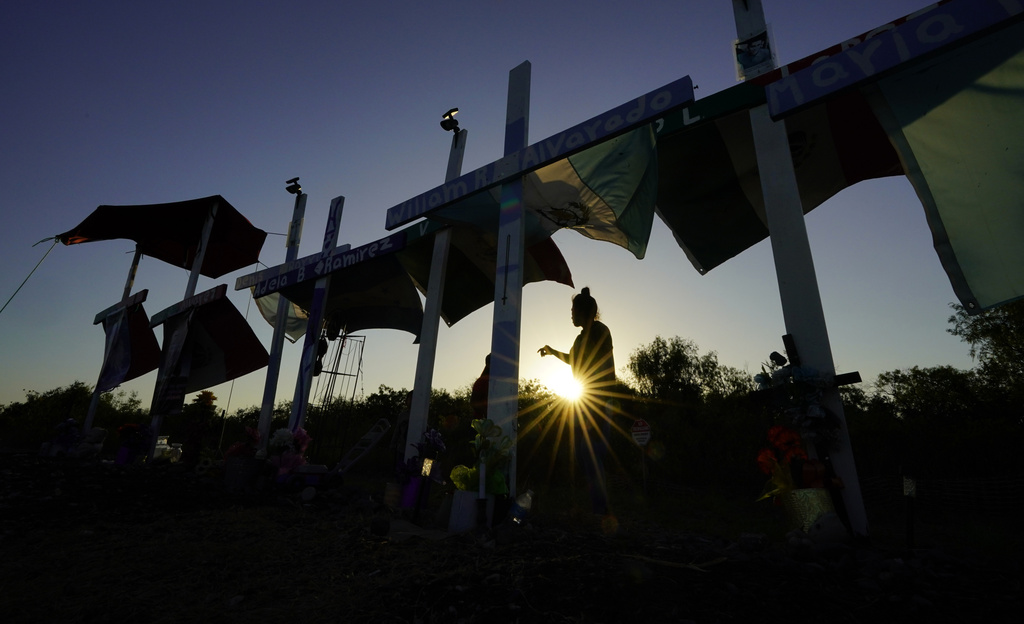 A woman walks along some of the 53 crosses that are part of a makeshift memorial at the site where officials found dozens of people dead in an abandoned semitrailer containing suspected migrants last summer, Tuesday, June 27, 2023, in San Antonio. U.S. authorities announced the arrests of four more people in connection to the smuggling deaths of 53 migrants, including eight children, who were left in a tractor trailer in the scorching Texas summer. (AP Photo/Eric Gay)