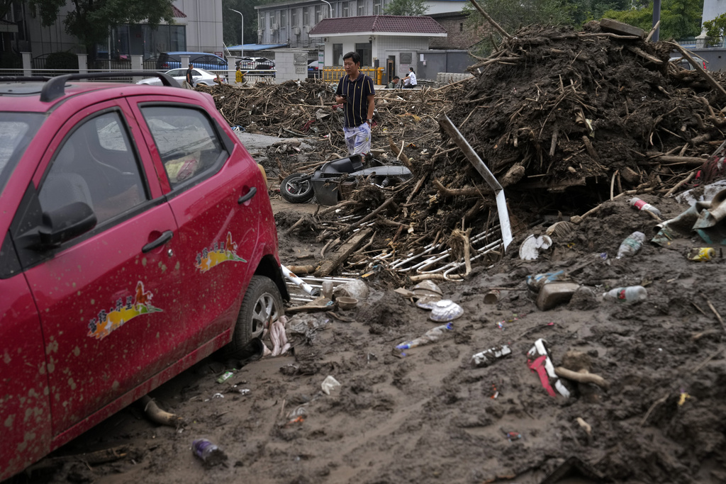 A man walks by damaged vehicles left over with the floods debris clogged on a street in the aftermath of flood waters from an overflowing river in the Mentougou district on the outskirts of Beijing on Monday, Aug. 7, 2023. The death toll in recent flooding in China's capital rose, officials said Wednesday, as much of the country's north remains threatened by unusually heavy rainfall. (AP Photo/Andy Wong)