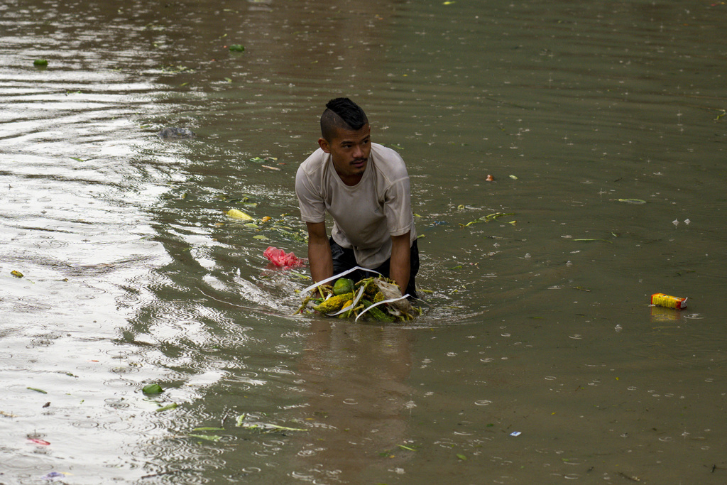 A man collects vegetable from water after heavy monsoon rains flooded a vegetable market in Kathmandu, Nepal, Tuesday, Aug. 8, 2023. (AP Photo/Niranjan Shrestha)