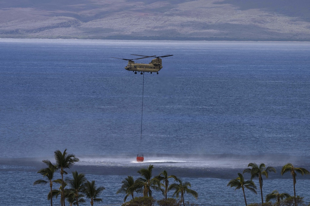 A Chinook helicopter scoops up water from the ocean near Lahaina, Hawaii, Wednesday, Aug. 16, 2023. Public schools on Maui started the process of reopening and traffic resumed on a major road in signs of recovery a week after wildfires demolished a historic town and killed at least 110 people, while the head of the island's emergency agency said he had 