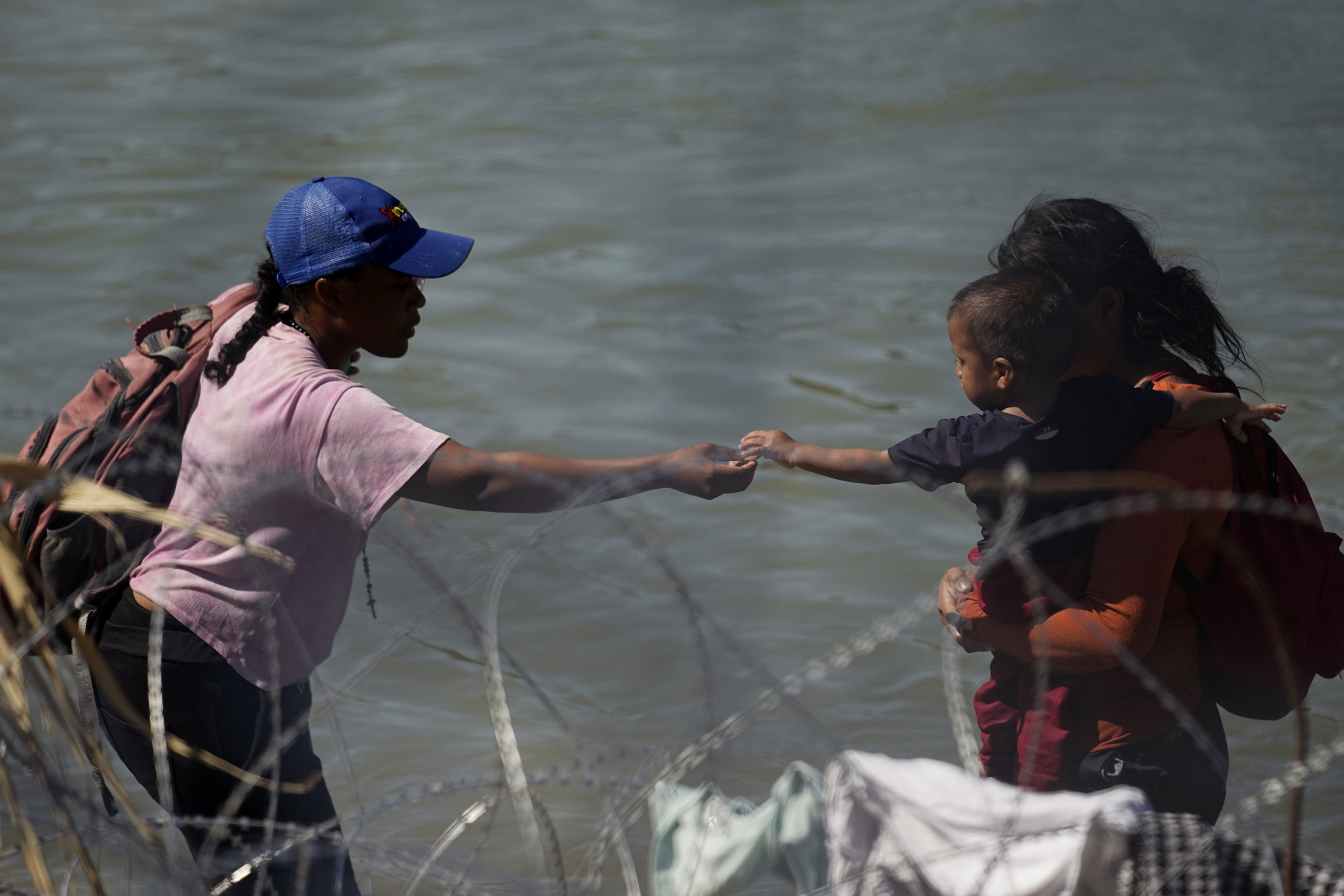 A young boy is passed food as migrants who crossed into the U.S. from Mexico are met with concertina wire along the Rio Grande, Thursday, Sept. 21, 2023, in Eagle Pass, Texas. (AP Photo/Eric Gay)