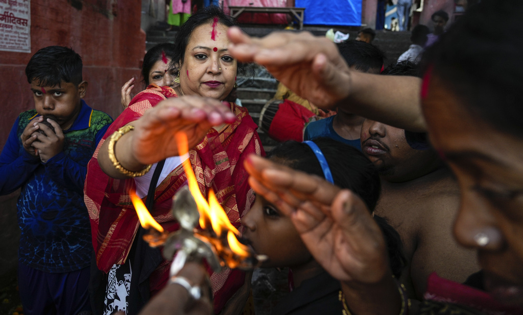 Hindu devotees take warmth of an oil lamp as blessings on the first day of Durga Puja festival on the banks of the Hooghly River in Kolkata, India, Saturday, Oct. 21, 2023. The five-day festival commemorates the slaying of a demon king by goddess Durga, marking the triumph of good over evil. (AP Photo/Bikas Das)