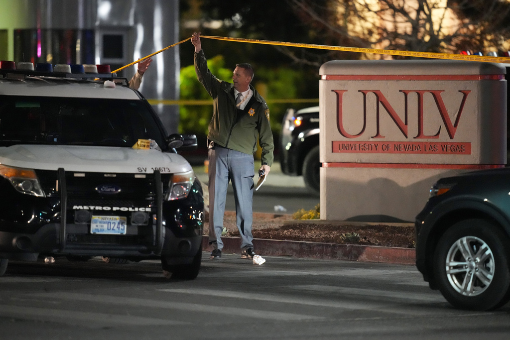 A police officer walks under crime scene tape in the aftermath of a shooting at the University of Nevada, Las Vegas, Wednesday, Dec. 6, 2023, in Las Vegas. (AP Photo/John Locher)