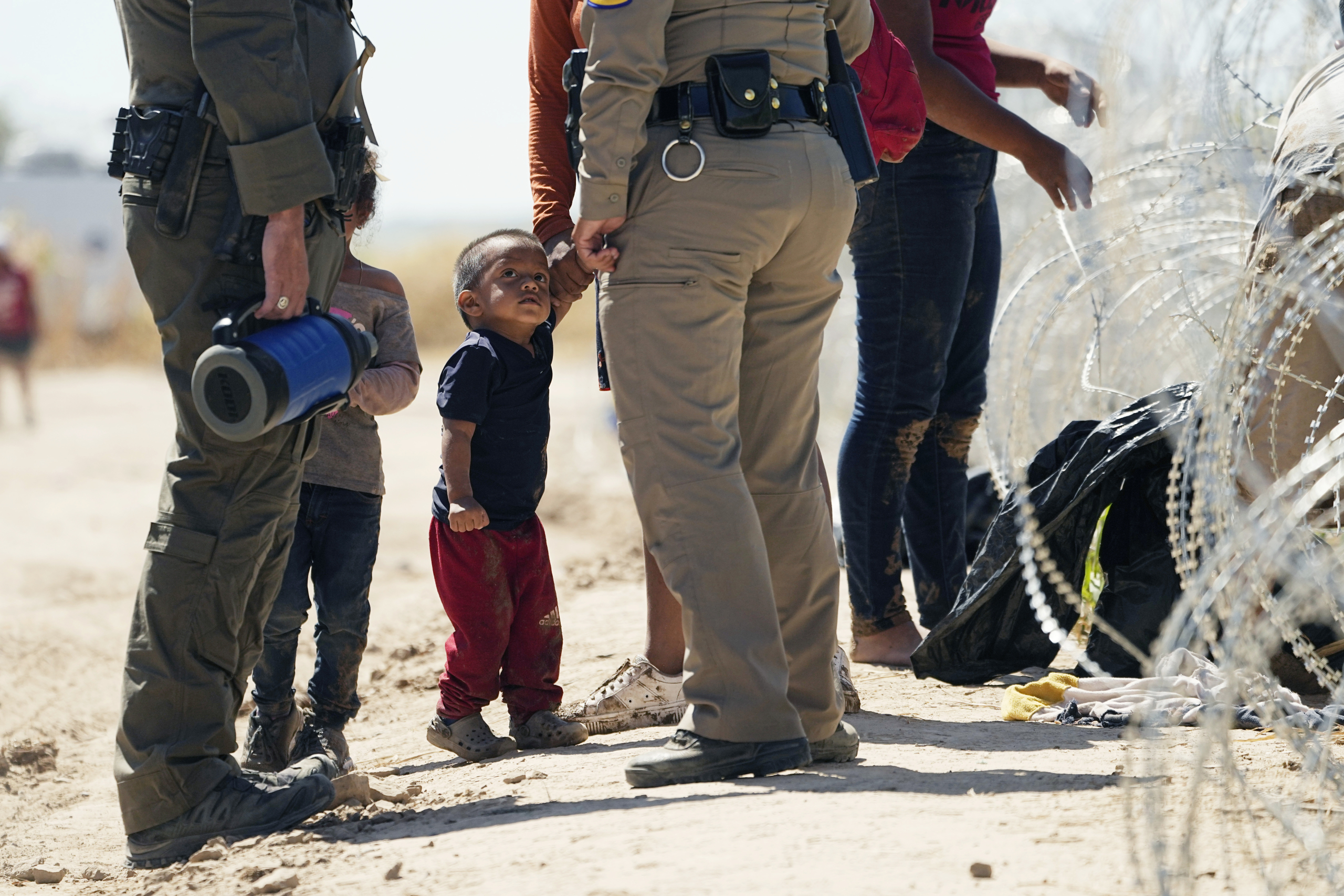 Migrants who crossed into the U.S. from Mexico passing under concertina wire are are met by law enforcement along the Rio Grande, Thursday, Sept. 21, 2023, in Eagle Pass, Texas. (AP Photo/Eric Gay)