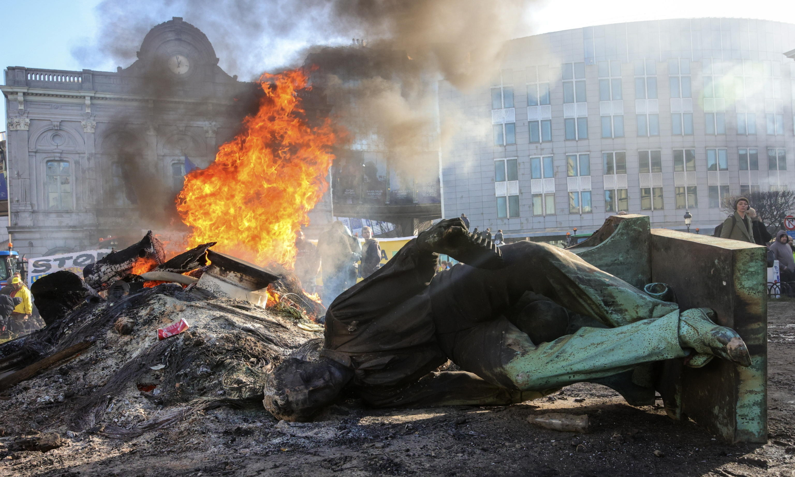 epa11117971 A statue lies on the ground as a fire burns during a farmers' protest in front of the European Parliament on the sidelines of a EU summit in Brussels, Belgium, 01 February 2024. Several hundred tractors are expected to converge on Brussels on the sidelines of a European leaders' summit on 01 February, the Walloon Federation of Agriculture (FWA) announced. Farmers are protesting to highlight their declining incomes, overly complex legislation and administrative overload. The discontent among farmers, initially sparked in France, has spilled over into several European countries, including Belgium, particularly in the Walloon region.  EPA/OLIVIER MATTHYS