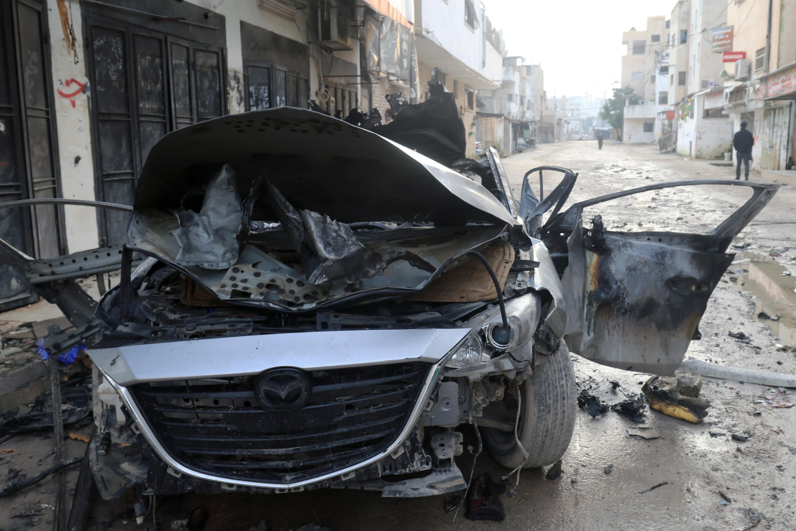 epa11174114 A destroyed car sits on a street following strikes by the Israeli army in Jenin, West Bank, 23 February 2024. Two Palestinians were killed and 14 wounded during an overnight Israeil airstrike in Jenin's refugee camp, according to the Palestinian health ministry. More than 29,400 Palestinians and over 1,300 Israelis have been killed, according to the Palestinian Health Ministry and the Israel Defense Forces (IDF), since Hamas militants launched an attack against Israel from the Gaza Strip on 07 October 2023, and the Israeli operations in Gaza and the West Bank which followed it.  EPA/ALAA BADARNEH