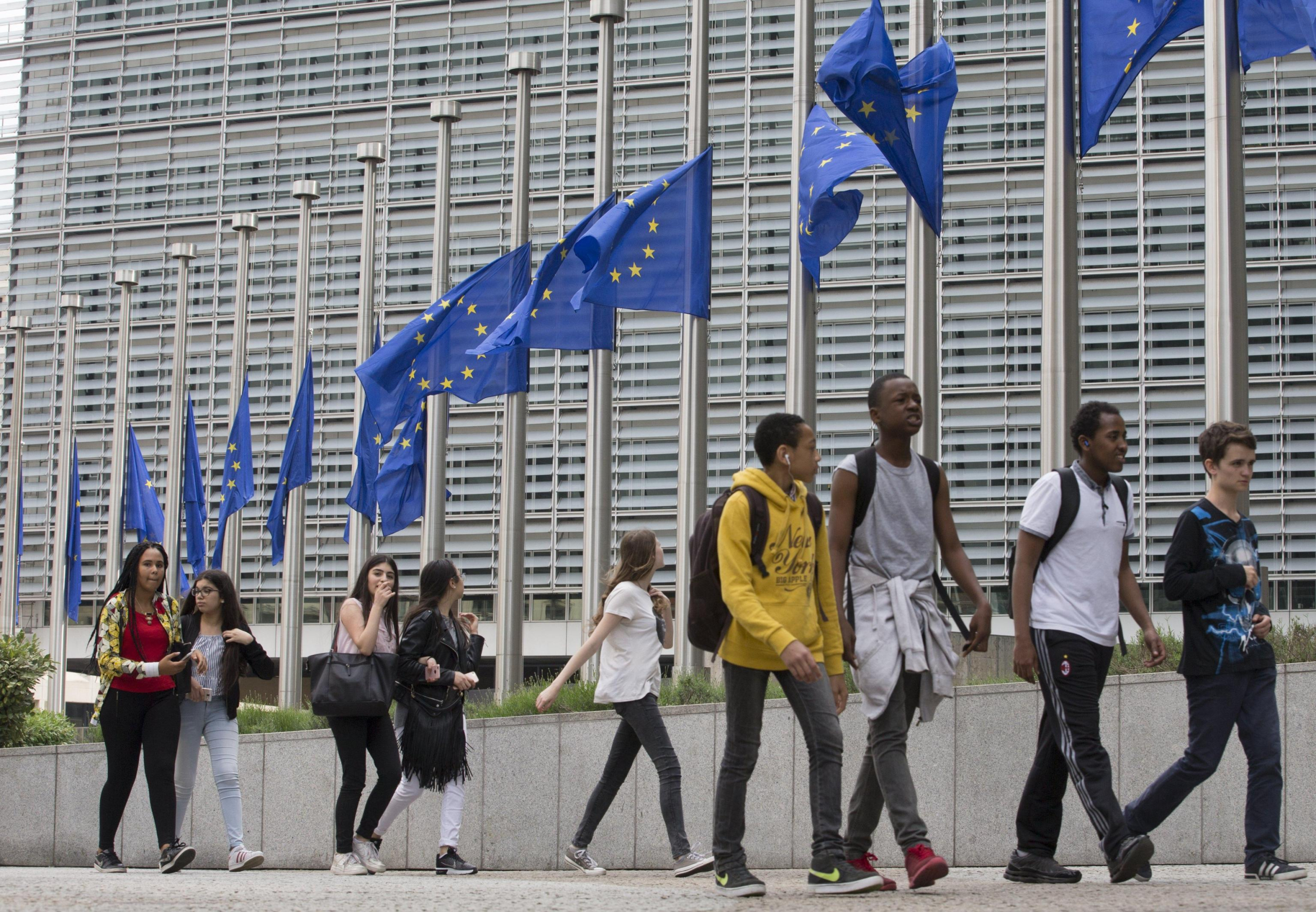 Un gruppo di giovani cammina davanti alle bandiere dell'Unione europea abbassate a mezz'asta fuori dall'edificio che ospita la sede della Commissione europea, a Bruxelles, in Belgio. (Foto ANSA, EPA/OLIVIER HOSLET)