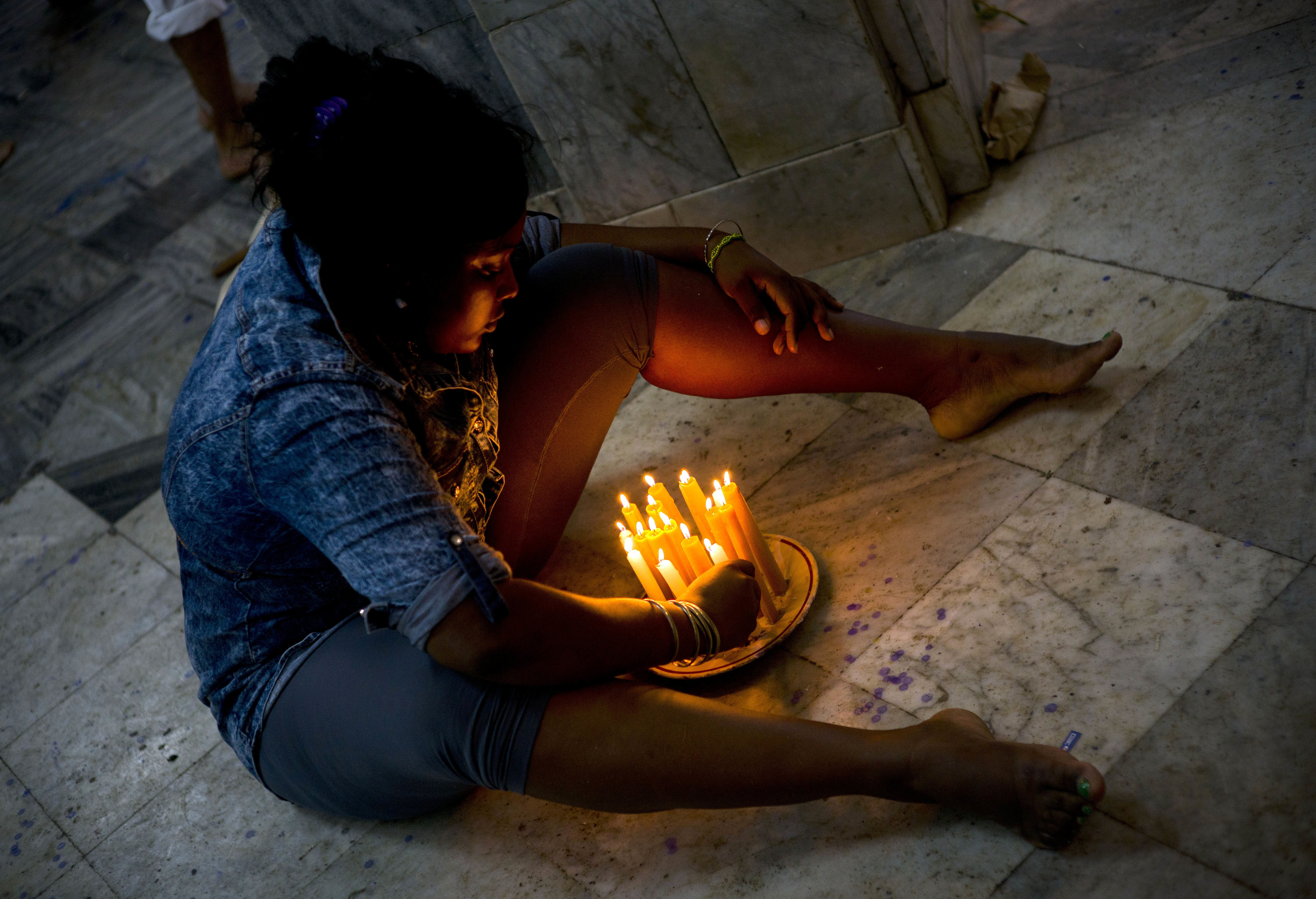 Wirnea, who declined to give her last name, lights a plate of candles on the church floor as she ends her pilgrimage to Saint Lazarus' shrine in El Rincon, an area of Santiago de las Vegas, Cuba, late Friday, Dec. 16, 2016. Wirnea said she came to thank the saint for granting her health-related request made on her first pilgrimage last year. The Catholic saint is also known as the Afro-Cuban Yoruba deity Babalu-Aye, protector of the sick, an example of Cuba's religions syncretism. His feast day is every Dec. 17. (AP Photo/Ramon Espinosa)