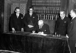 Il presidente della repubblica Enrico De Nicola firma la costituzione italiana alla presenza di Alcide De Gasperi e Umberto Terracini. 