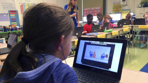 In this Sept. 20, 2018 photo, fifth grade student Ashlynn De Filippis, left, works math problems on the DreamBox system as teacher Heather Dalton, center rear, works with other students in class at Charles Barnum Elementary School in Groton, Conn. A wide array of apps, websites and software used in schools borrow elements from video games to help teachers connect with students living technology-infused lives. (AP Photo/Michael Melia)
