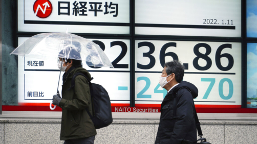 People wearing protective masks walk in front of an electronic stock board showing Japan's Nikkei 225 index at a securities firm Tuesday, Jan. 11, 2022, in Tokyo. Asian shares sank in cautious trading Tuesday following a decline on Wall Street amid continuing worries about the omicron coronavirus variant, especially rising cases in China. (AP Photo/Eugene Hoshiko)