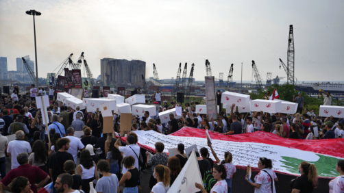 People hold symbolic coffins outside the port to mark the second anniversary of the massive blast at Beirut's port in Beirut, Lebanon, Thursday, Aug. 4, 2022. A large block of Beirut's giant port grain silos, shredded by a massive explosion two years ago, collapsed on Thursday as hundreds marched in the Lebanese capital to mark the anniversary of the blast that killed scores. (AP Photo/Hassan Ammar)