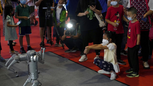 A child wearing a face mask gestures as she plays with a Unitree Go 1 intelligent side-follow robot during the World Robot Conference at the Yichuang International Conference and Exhibition Centre in Beijing, Thursday, Aug. 18, 2022. (AP Photo/Andy Wong)