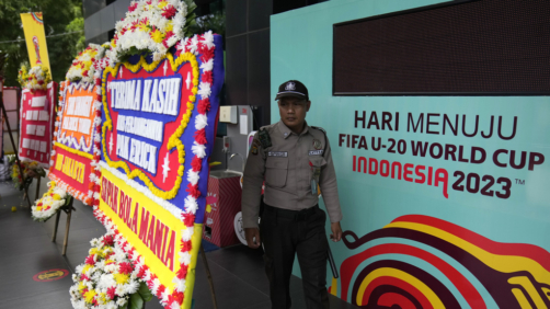 A security guard walks between a banner of FIFA U-20 World Cup and condolence wreaths sent by soccer supporters, outside the building housing the office of Indonesian Soccer Association, PSSI, in Jakarta, Indonesia, Thursday, March 30, 2023. Indonesia was stripped of hosting rights for the Under-20 World Cup on Wednesday only eight weeks before the start of the tournament amid political turmoil regarding Israel's participation. (AP Photo/Dita Alangkara)