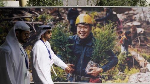People walk past a poster ahead of the COP28 U.N. Climate Summit, Wednesday, Nov. 29, 2023, in Dubai, United Arab Emirates. (AP Photo/Rafiq Maqbool)