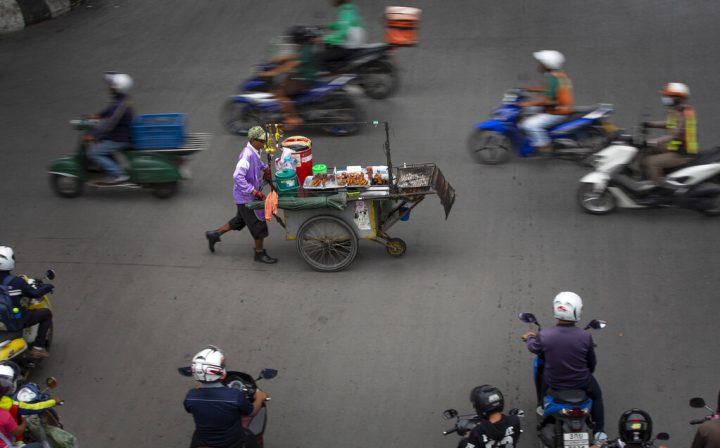 Un venditore ambulante spinge un carrello portavivande in un incrocio trafficato a Bangkok, in Thailandia