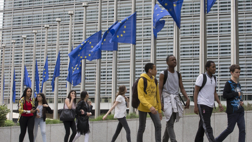 Un gruppo di giovani cammina davanti alle bandiere dell'Unione europea abbassate a mezz'asta fuori dall'edificio che ospita la sede della Commissione europea, a Bruxelles, in Belgio. (Foto ANSA, EPA/OLIVIER HOSLET)